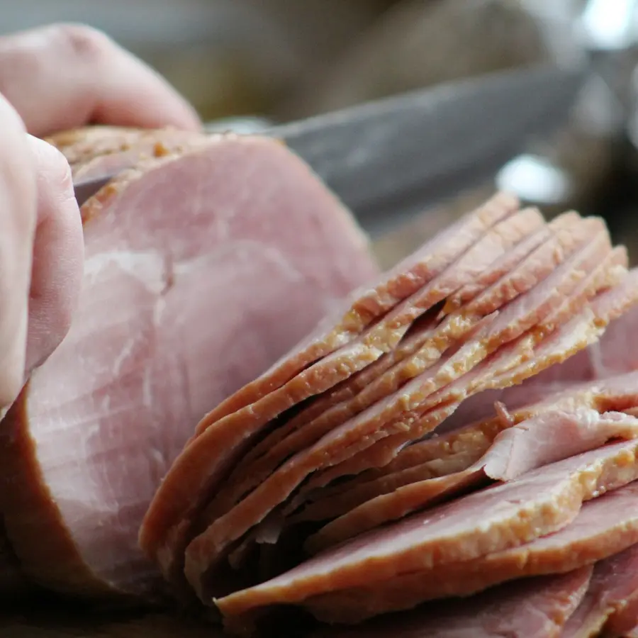 Manos cortando jamón cocido con un cuchillo largo